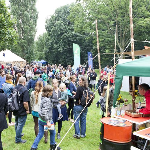 Menschen laufen &uuml;ber eine Wiese. Um sie herum stehen Zelte.