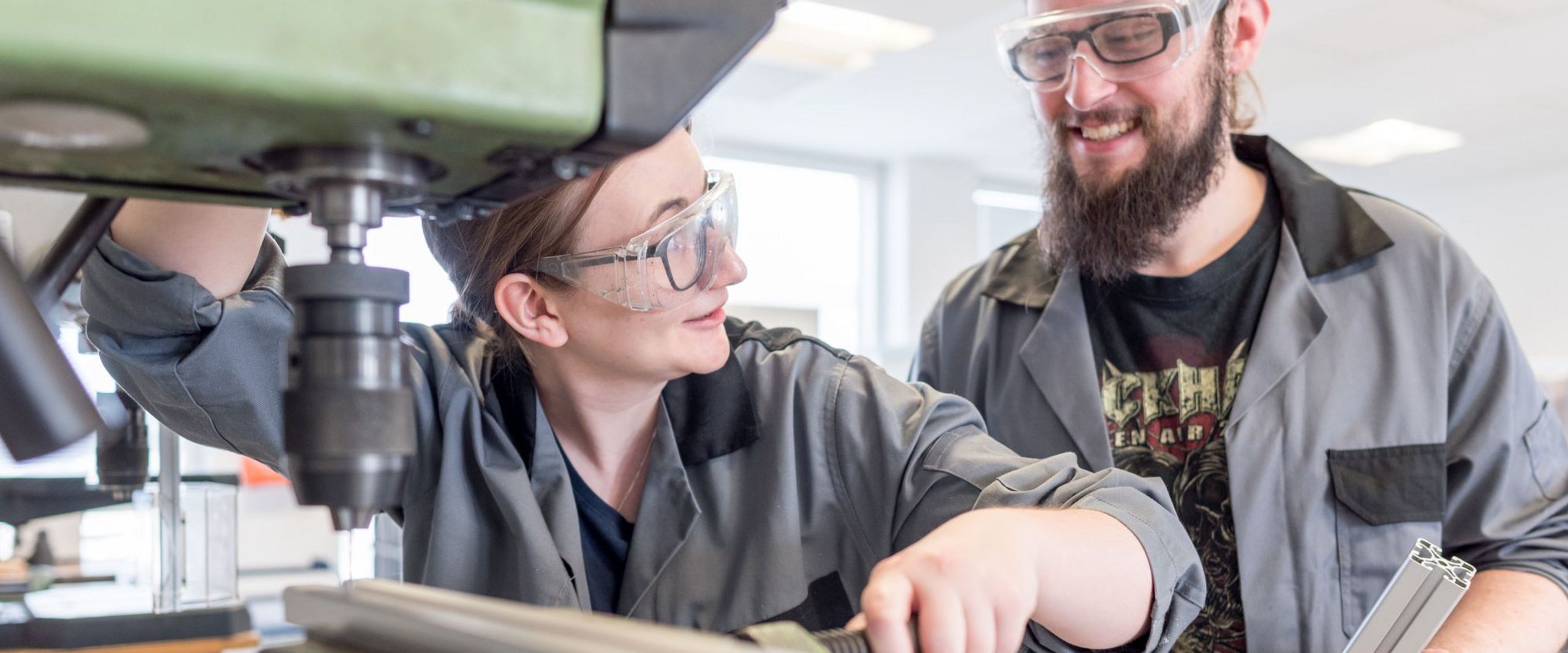 Eine Studentin spannt eine Metallstange in eine Maschine ein, während ein zweiter Student ihr dabei zusieht.