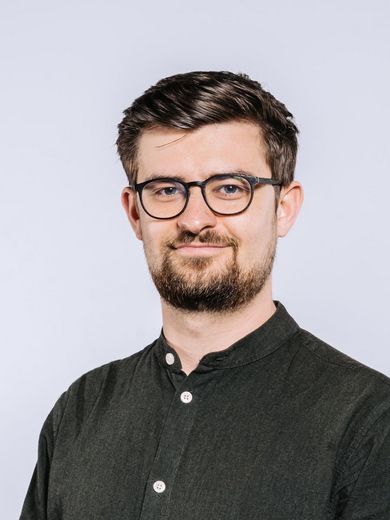 Auf dem Bild ist Milan Sixt zu sehen. Er trägt ein dunkles Hemd und kurze dunkle Brille. 