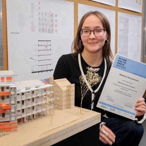 Junge Frau hält Urkunde und steht vor einem kleinen Holzmodell