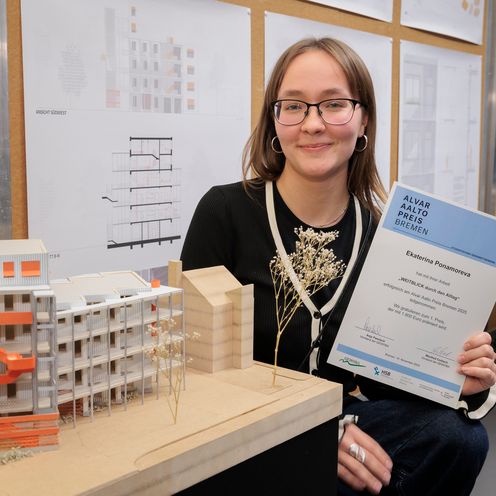 Junge Frau hält Urkunde und steht vor einem kleinen Holzmodell