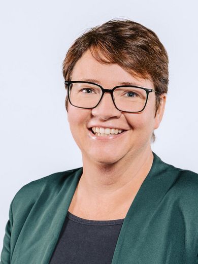 Auf dem Bild ist Ilka Gaulke zusehen. Sie hat kurze braune Haare und trägt einen grünen Blazer über einem schwarzen T-Shirt. Außerdem trägt sie eine Brille. 