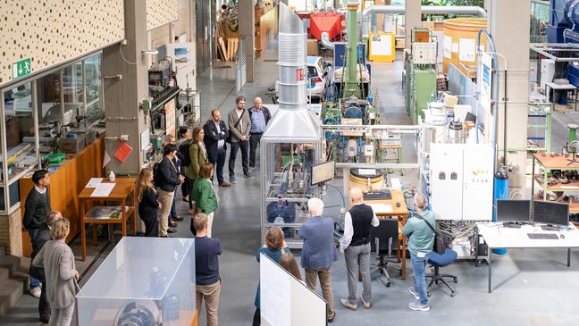 Auf dem Bild ist eine Gruppe Leute fotografiert, die sich um einen Elektrolyseur versammelt haben. Das Bild ist aus der Vogelperspektive aufgenommen. 