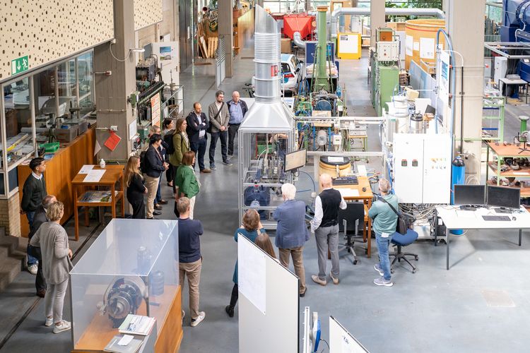 Auf dem Bild ist eine Gruppe Leute fotografiert, die sich um einen Elektrolyseur versammelt haben. Das Bild ist aus der Vogelperspektive aufgenommen. 