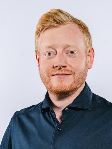 Auf dem Foto ist Albert Ulbertus zusehen. Er hat kurzes rötliches Haar und einen Bart. Er trägt ein dunkelblaues Hemd.