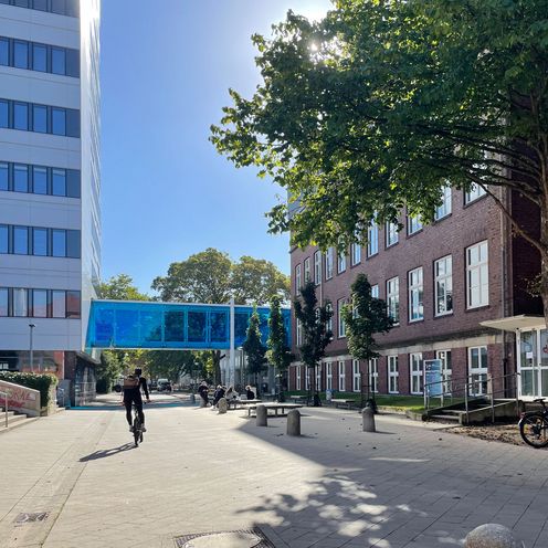 Geb&auml;ude und Sta&szlig;e mit &Uuml;bergang. Radfahrer und Fu&szlig;g&auml;nger sind zu sehen.
