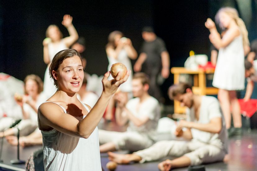 Bühnenszene aus dem Theaterstück "Peer Gynt". Im Vordergrund steht eine junge Frau, die eine Kugel hochhält.