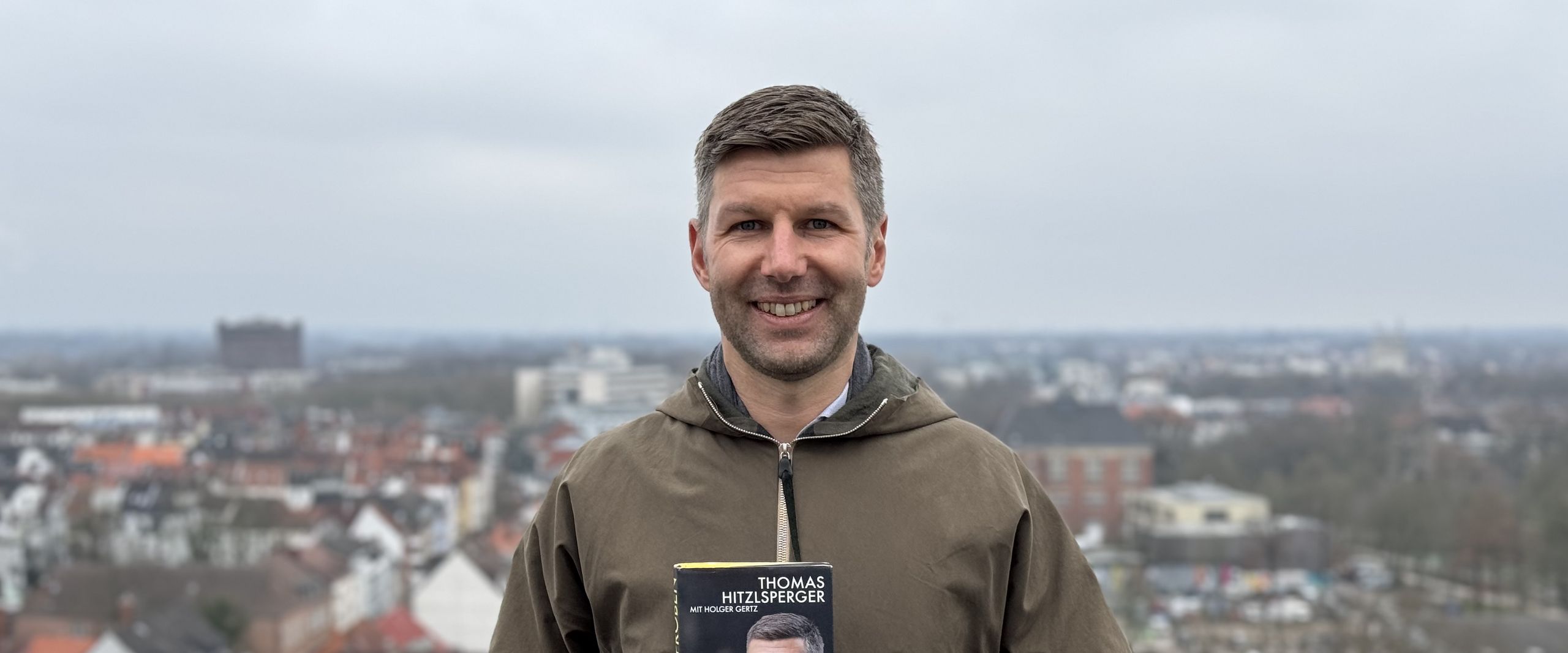 Mann h&auml;lt Buch und lacht in die Kamera