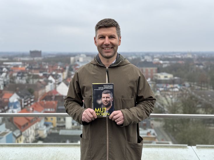 Mann h&auml;lt Buch und lacht in die Kamera