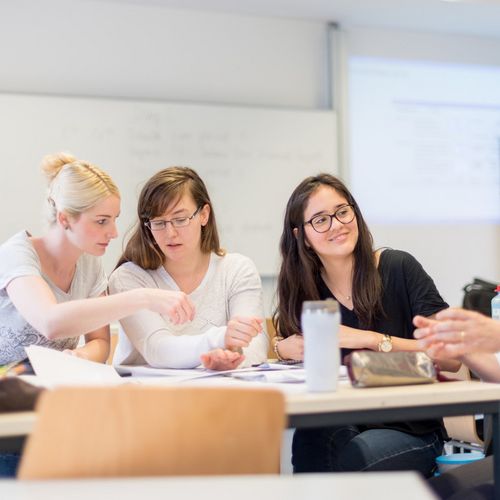 f&uuml;nf HSB Studierende sitzen zusammen an einem Tisch und arbeiten gemeinsam. Mit ihnen am Tisch sitzt eine Lehrperson. 