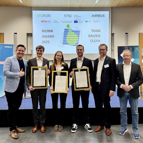Gruppenbild mit Männern und Frau. Drei Personen halten eine gerahmte Urkunde.