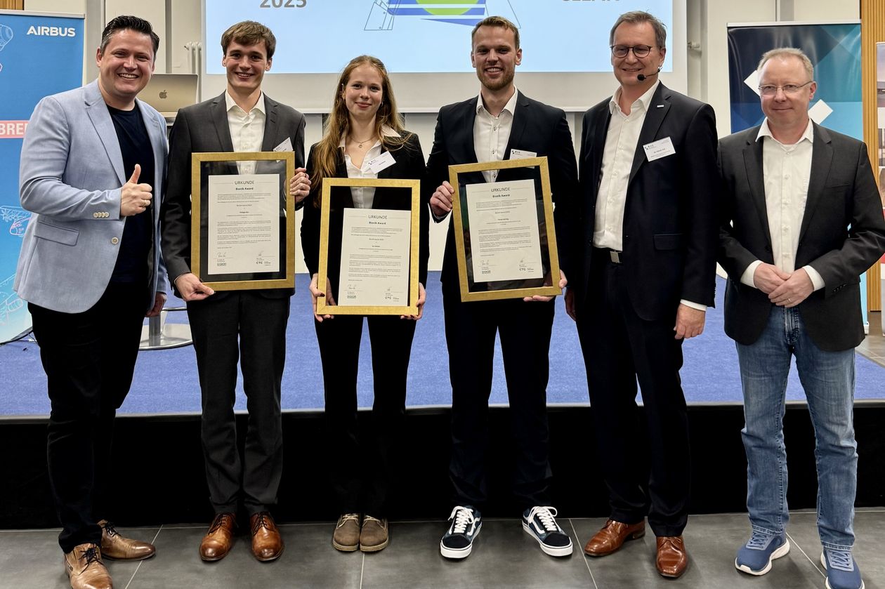 Gruppenbild mit Männern und Frau. Drei Personen halten eine gerahmte Urkunde.