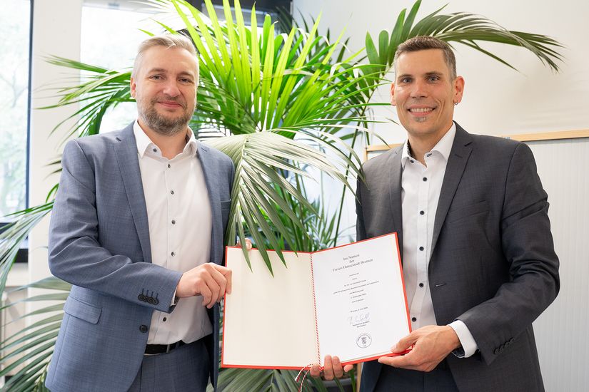 Prof. Dr. Dr. Jan Thiele mit Kanzler der HSB, beide halten die Ernennungsurkunde in ihrer Mitte
