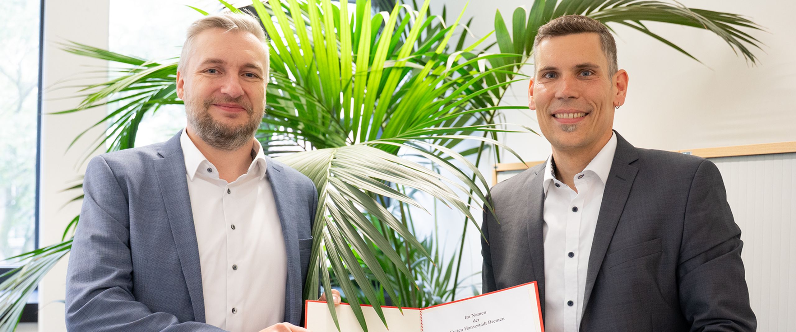 Prof. Dr. Dr. Jan Thiele mit Kanzler der HSB, beide halten die Ernennungsurkunde in ihrer Mitte