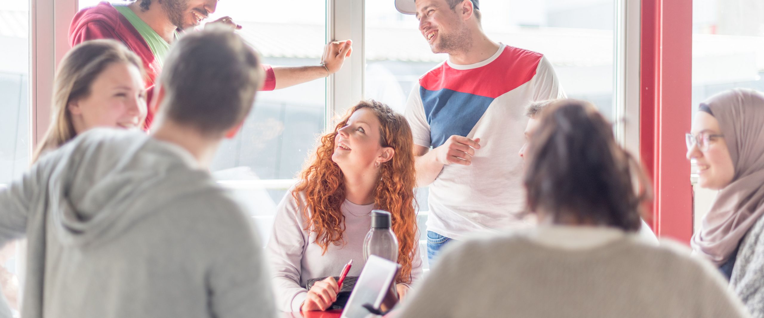 Eine Gruppe von Studierenden unterhält sich, einige stehen, andere sitzen. 
