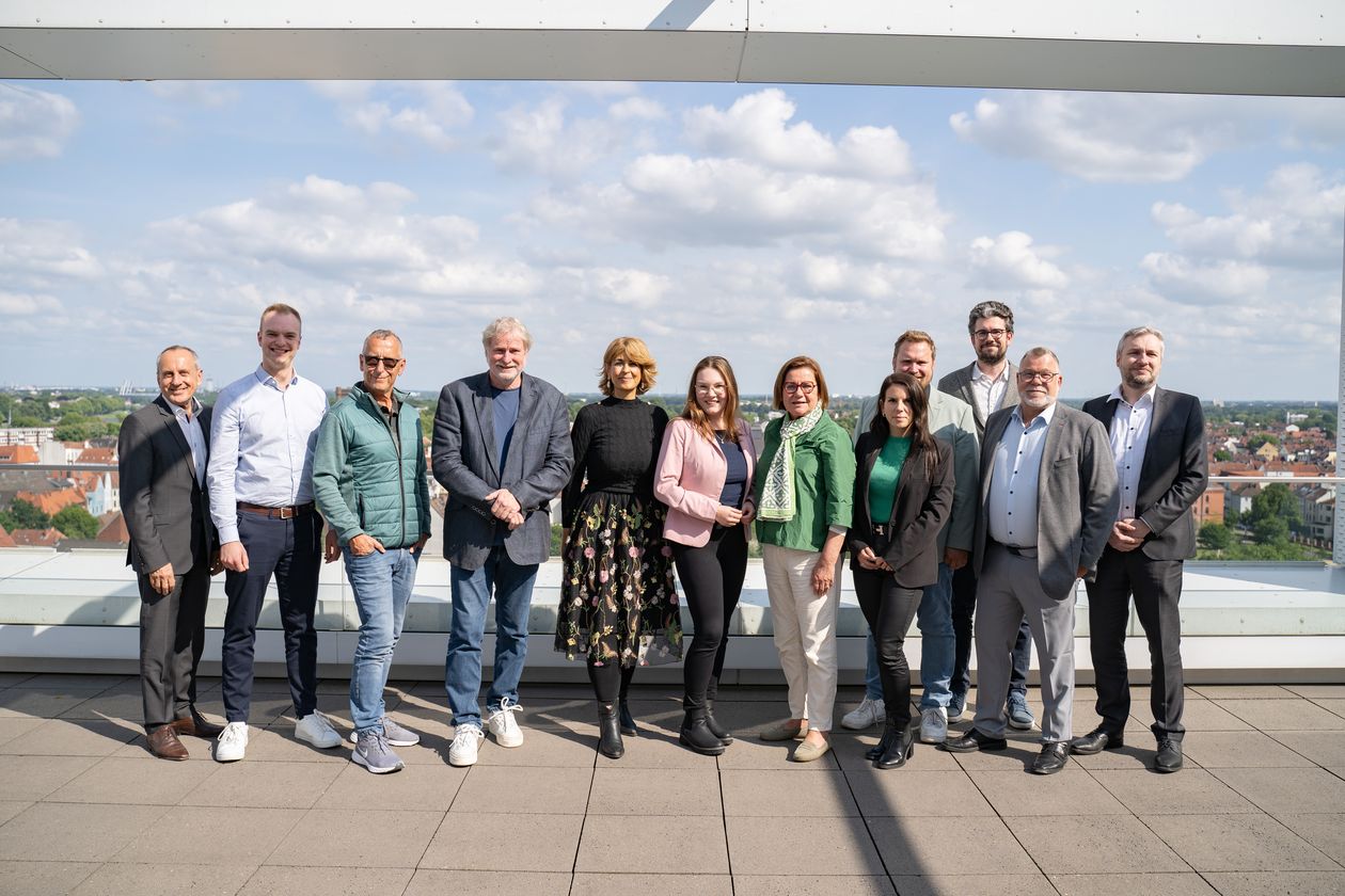 Auf dem Foto sind 10-12 Personen in einer Reihe aufgestellt. Im Hintergrund ist die Skyline von Bremen zu erkennen. Die Personen stehen auf der Dachterasse. 