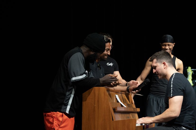 mann sitzt am Klavier und spielt. Andre stehen dabei.