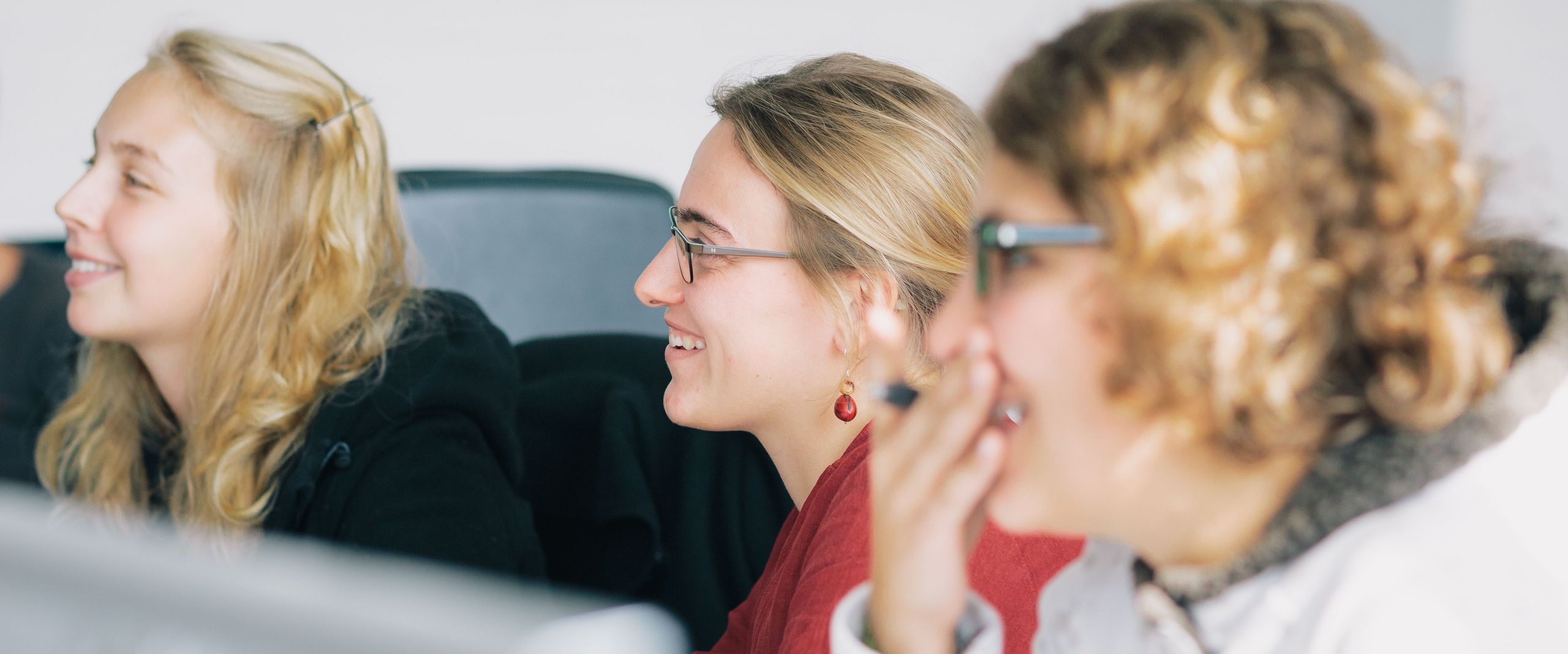 3 Studentinnen sitzen vor einem Bildschirm, sie lächeln