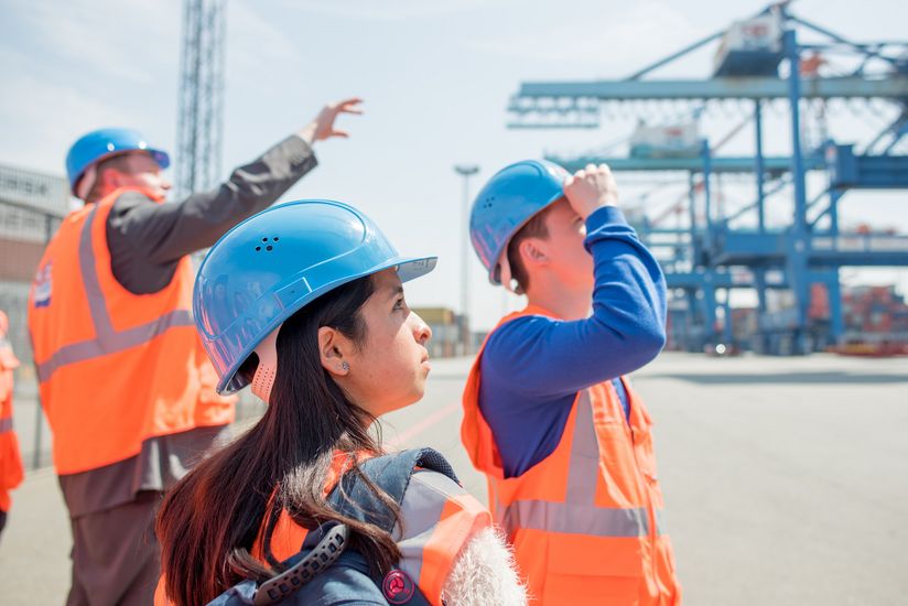 Exkursion zum Containerterminal Ein Beschäftigter führt Studierende in Warnwesten und Schutzhelmen durch ein Containerterminal.