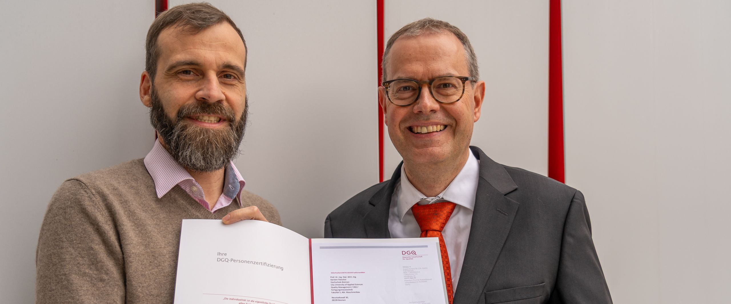 Zwei M&auml;nner halten eine Urkunde und lachen in die Kamera