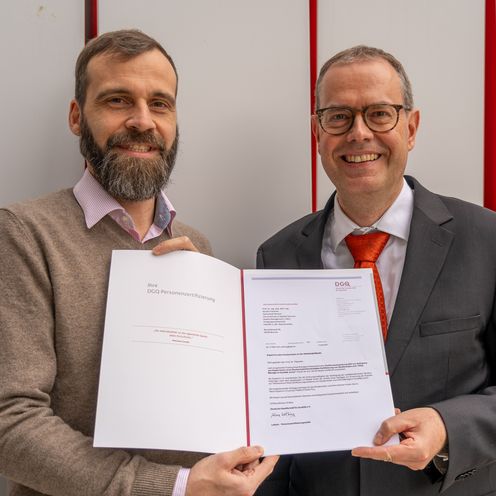 Zwei M&auml;nner halten eine Urkunde und lachen in die Kamera