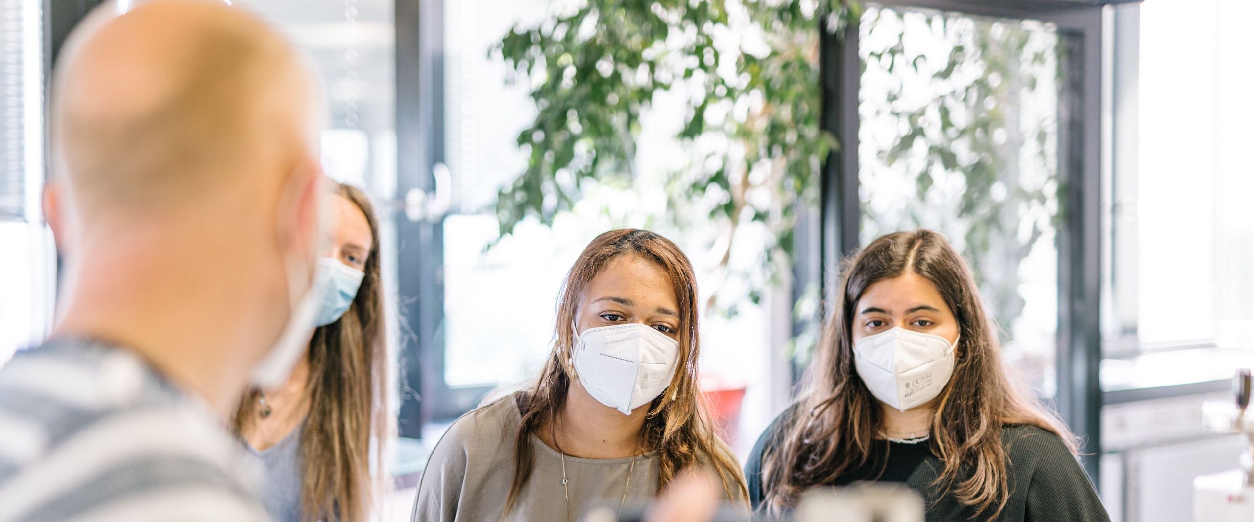 Zwei Studierende mit Masken hören dem Professor zu.