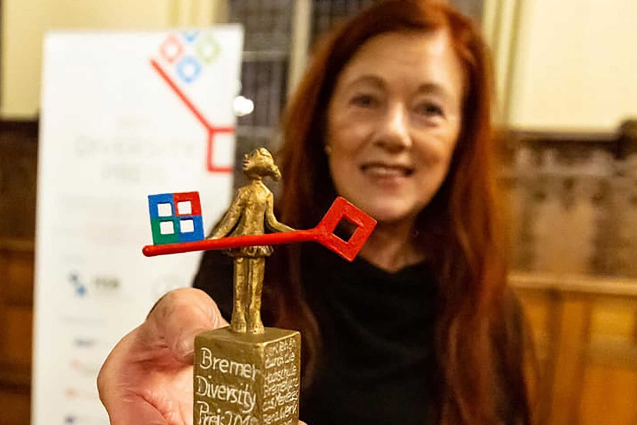 Frau hält Skulptur in die Kamera. Im Hintergrund sieht man ein Roll-up