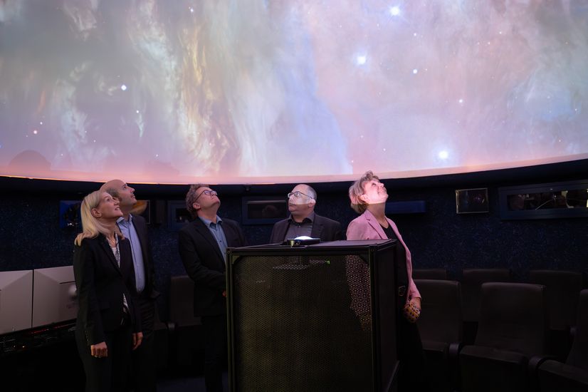 Drei Männer und zwei Frauen blicken im Dunkeln in den Sternenhimmel in einem Planetarium.