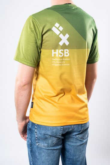Das Model trägt ein oversized Ombré T-Shirt in grün bis gelb für Herren mit dem HSB-Logo darauf und ist von hinten zu sehen.