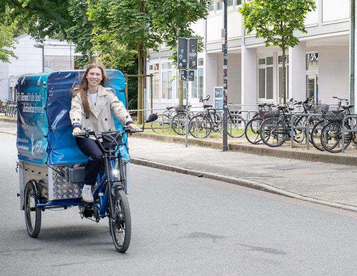 Studentin f&auml;hrt auf einem Lastenfahrrad auf einer Stra&szlig;e.