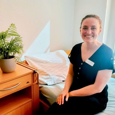 Frau sitzt auf einem Bett und lacht in die Kamera.