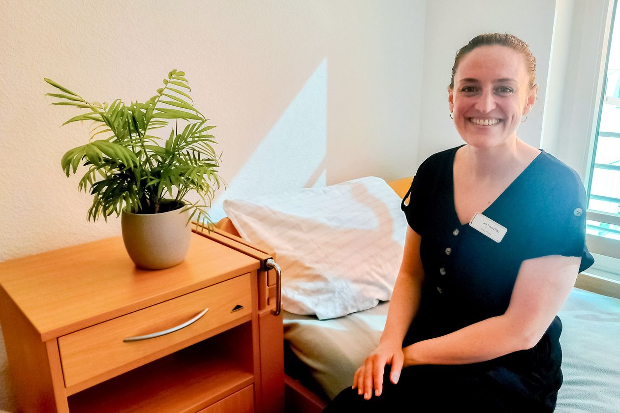 Frau sitzt auf einem Bett und lacht in die Kamera.