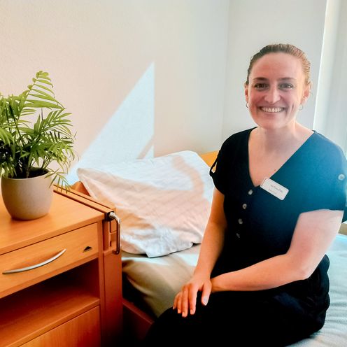 Frau sitzt auf einem Bett und lacht in die Kamera.