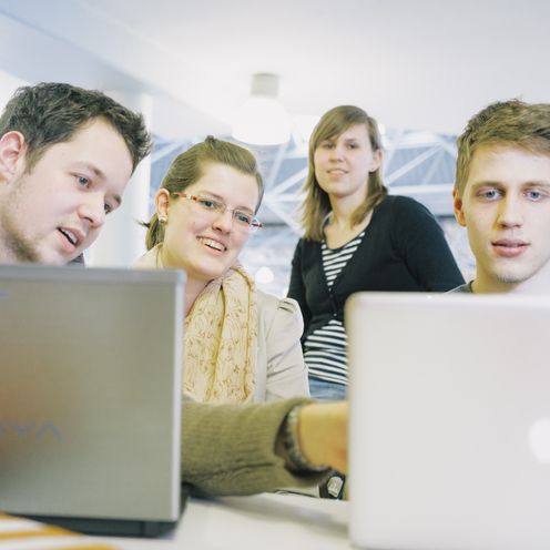 Junge M&auml;nner und Frauen schauen lachend auf Bildschirme