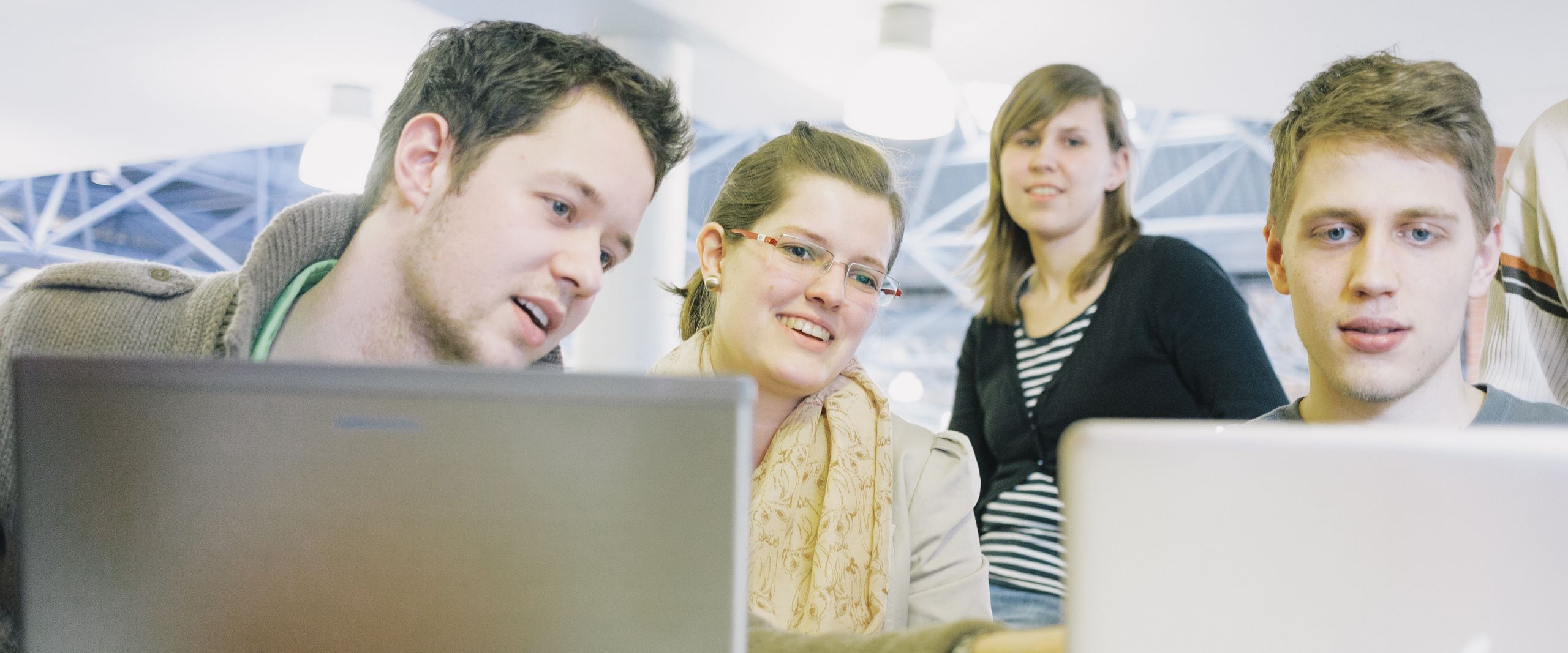 Junge M&auml;nner und Frauen schauen lachend auf Bildschirme