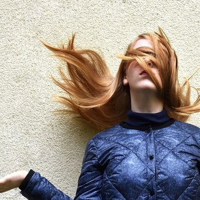 Frau mit langen Haaren, die ihr zum Teil im Gesicht hängen. Sie dreht eine Handinnenfläche nach oben.
