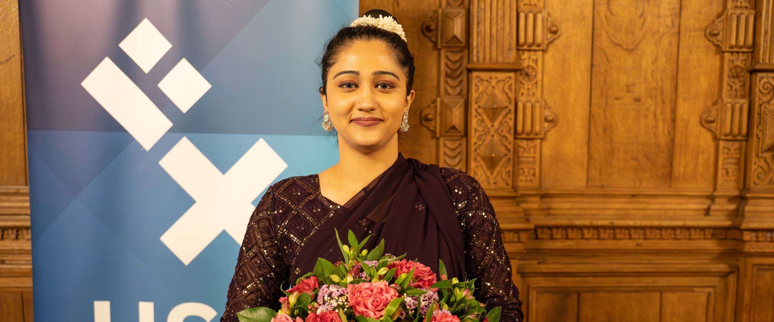 DAAD Prize winner 2025 Sannae Kapoor from Hochschule Bremen. Woman with flowers in front of a roll-up banner