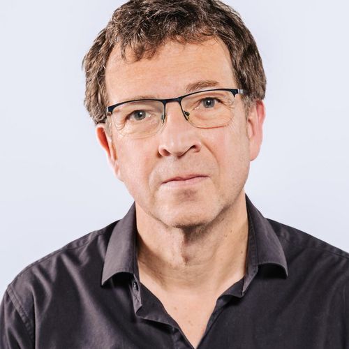 Auf dem Bild ist Windried Osthorst zusehen. Er hat kurze braune Haare und trägt ein schwarzes Hemd und eine Brille. 