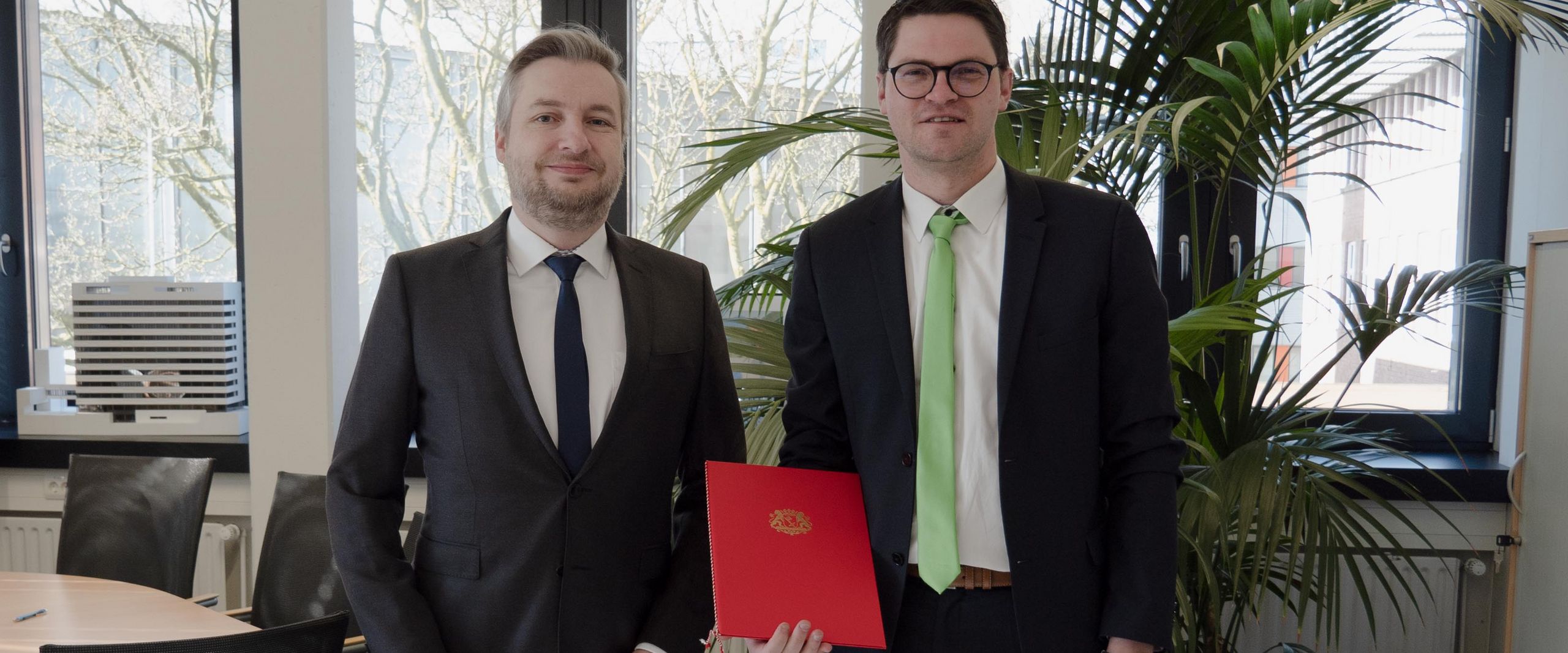 Zwei M&auml;nner l&auml;cheln in die kamera. Der rechte zeigt eine Urkunde.