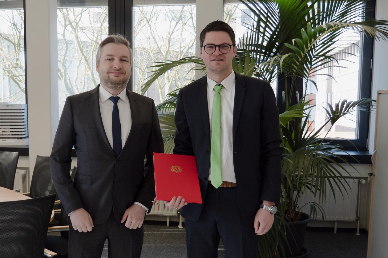 Zwei M&auml;nner l&auml;cheln in die kamera. Der rechte zeigt eine Urkunde.