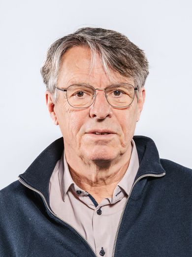 Auf dem Bild ist Felix Herle zusehen. Er hat kurzes dunkelgraues Haar und trägt eine dezente Brille. Außerdem hat er ein naturfarbenes Hemd unter einem dunkelblauen Strickjacke an. 