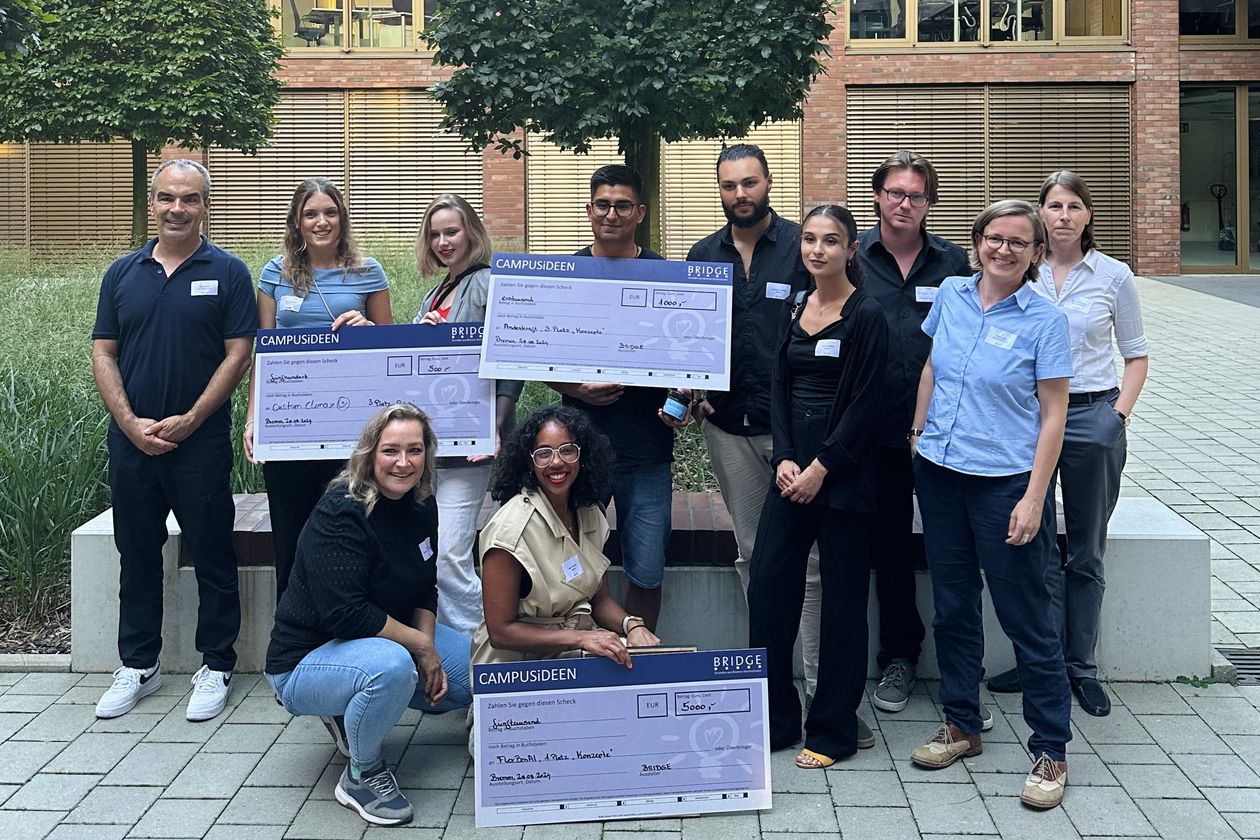 Gruppenbild mit M&auml;nnern und Frauen. Sie lachen und halten gro&szlig;e Checks hoch.