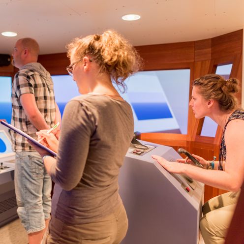 Drei Studierende sind auf ihren Posten auf der Br&uuml;cke im Schiffssimulator.