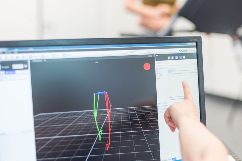 Übung Physiotherapie Eine Studentin läuft auf einem Laufband. Auf einem Bildschirm sind ihre Bewegungen ihrer Beine als Computeranimation zu sehen.