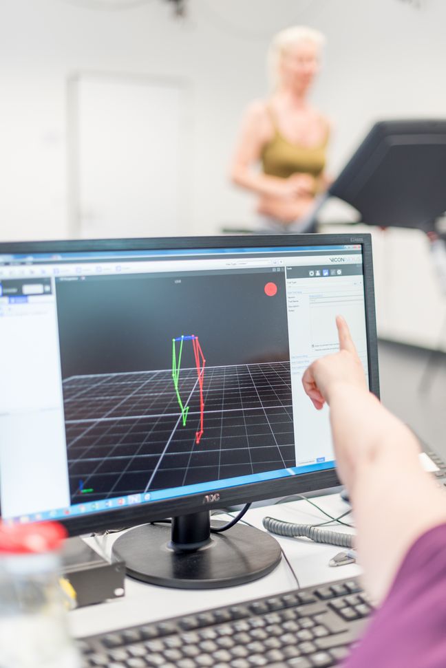 Eine Studentin läuft auf einem Laufband. Auf einem Bildschirm sind ihre Bewegungen ihrer Beine als Computeranimation zu sehen.