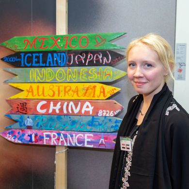 Zwei Studierende posieren neben einem Wegweiser, auf dem verschiedene Länder stehen.