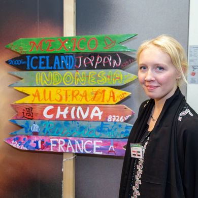 Zwei Studierende posieren neben einem Wegweiser, auf dem verschiedene Länder stehen.