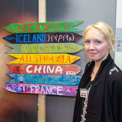 Zwei Studierende posieren neben einem Wegweiser, auf dem verschiedene Länder stehen.