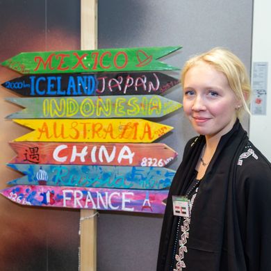 Zwei Studierende posieren neben einem Wegweiser, auf dem verschiedene Länder stehen.