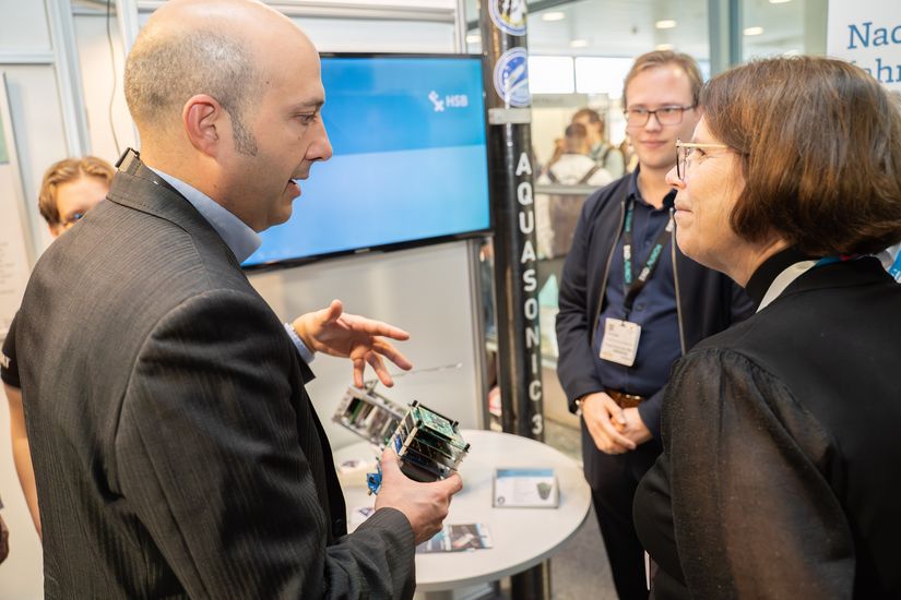 Mann spricht mit Frau und zeigt ihr kelinen Satelliten, den er in der Hand hält
